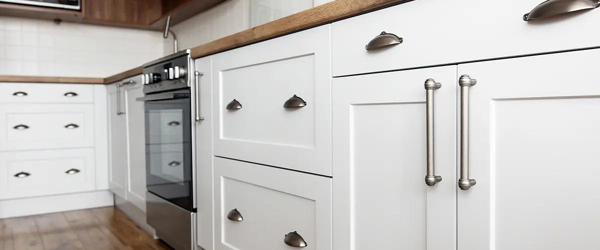 Stylish light gray handles on cabinets close-up, kitchen interior with modern furniture and stainless steel appliances.