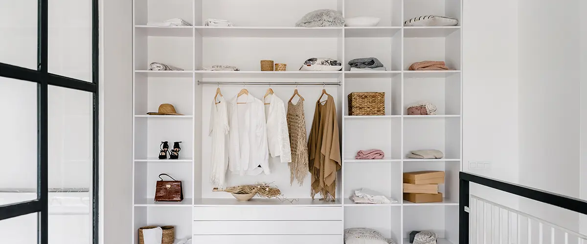 Minimalist open closet system in Cold Springs, with white shelving, hanging clothes, wicker baskets, and natural light on hardwood floors.