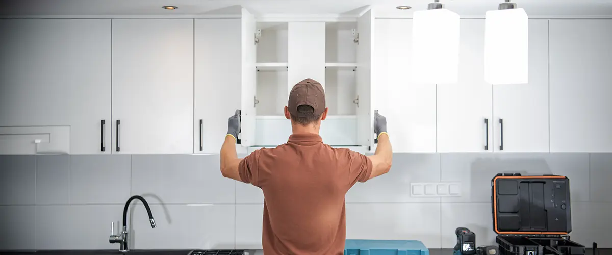 Professional kitchen cabinet maker in Cold Springs installing new cabinets, with a worker adjusting modern white cabinets in a contemporary kitchen.