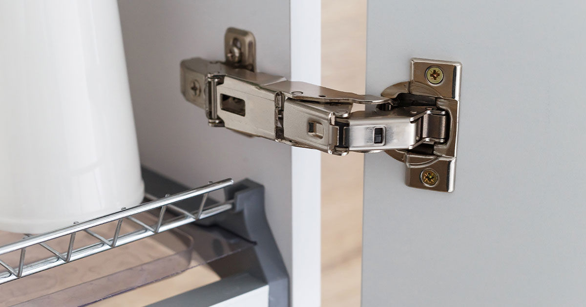 Close-up of a soft-close cabinet hinge mechanism on a white kitchen cabinet door for smooth and quiet operation.