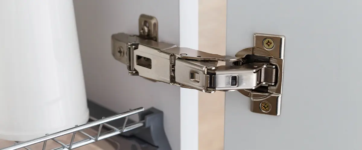 Cabinet hinge types. Close-up of a soft-close cabinet hinge mechanism on a white kitchen cabinet door for smooth and quiet operation.