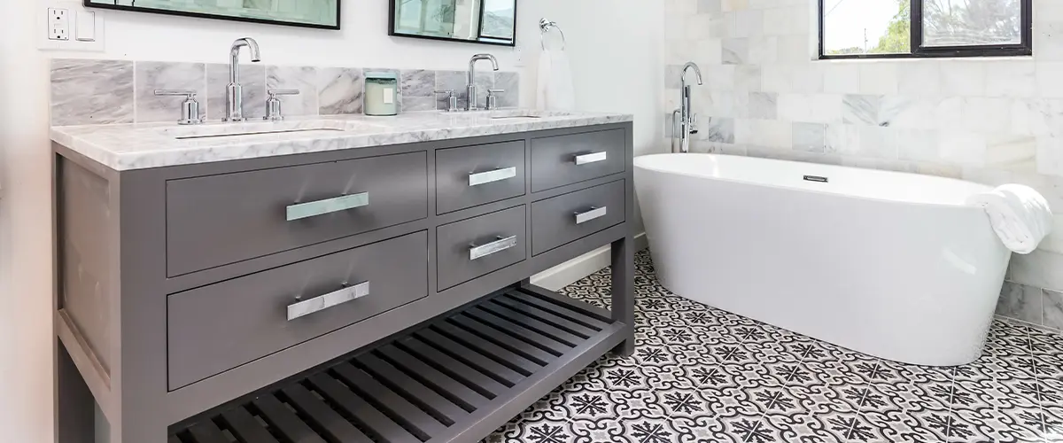 Modern gray bathroom with marble countertop, dual mirrors, freestanding tub and grey bathroom cabinets.