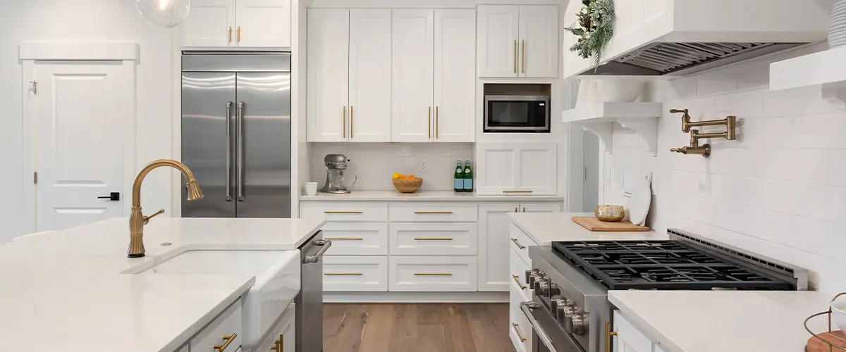 Bright white kitchen with gold hardware, farmhouse sink, marble countertops, and stainless steel appliances.