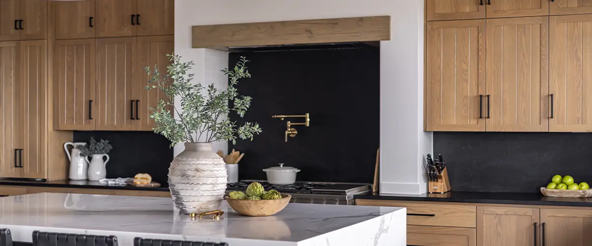 Modern kitchen with wood cabinetry, black backsplash, white marble island, and decorative pendant lighting.