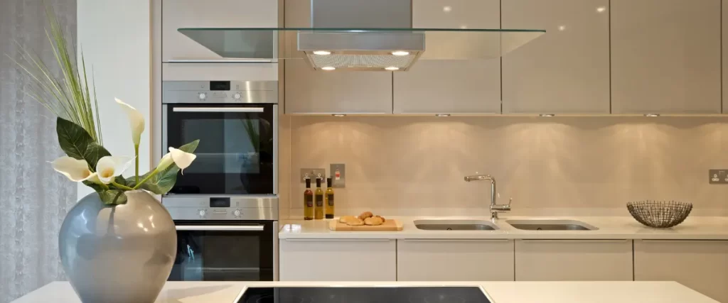 A modern kitchen with glossy beige cabinets, a glass range hood, stainless steel appliances, and a minimalist aesthetic