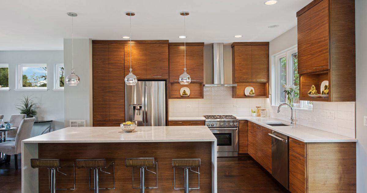 A modern kitchen with warm wood cabinetry, white quartz countertops, stainless steel appliances, and a spacious island with barstools