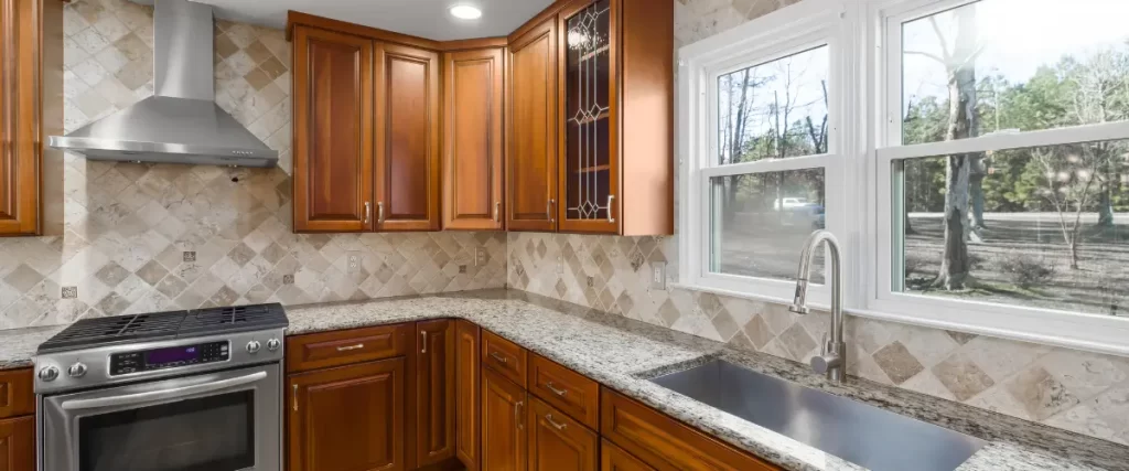  A traditional kitchen with warm wood cabinets, granite countertops, a large stainless steel sink, and a tiled backsplash