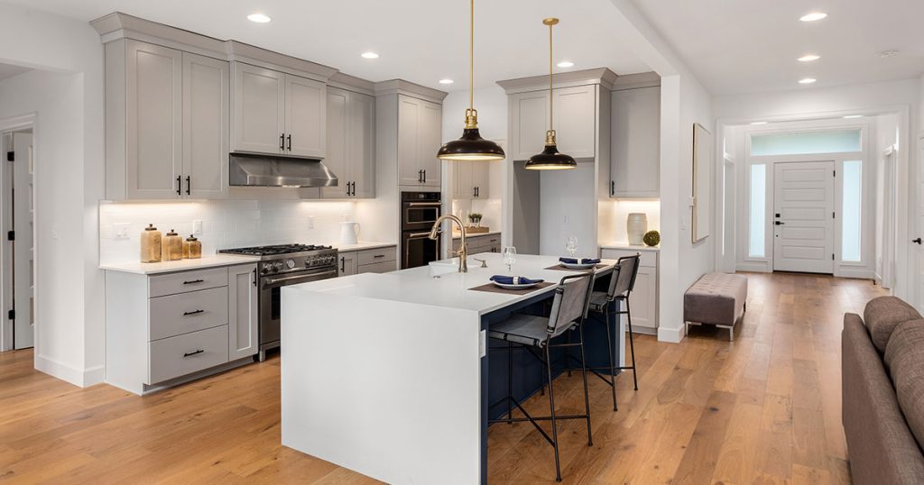 Contemporary kitchen with gray shaker cabinets, large island, gold pendant lighting, and hardwood floors.