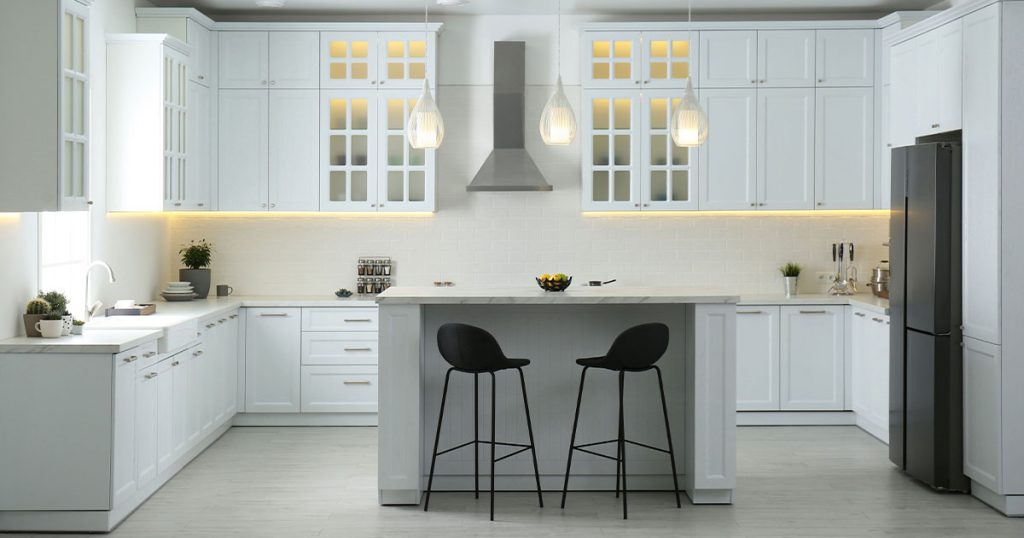 Luxury white kitchen with island seating, glass cabinets, stainless steel range hood, and modern pendant lighting.