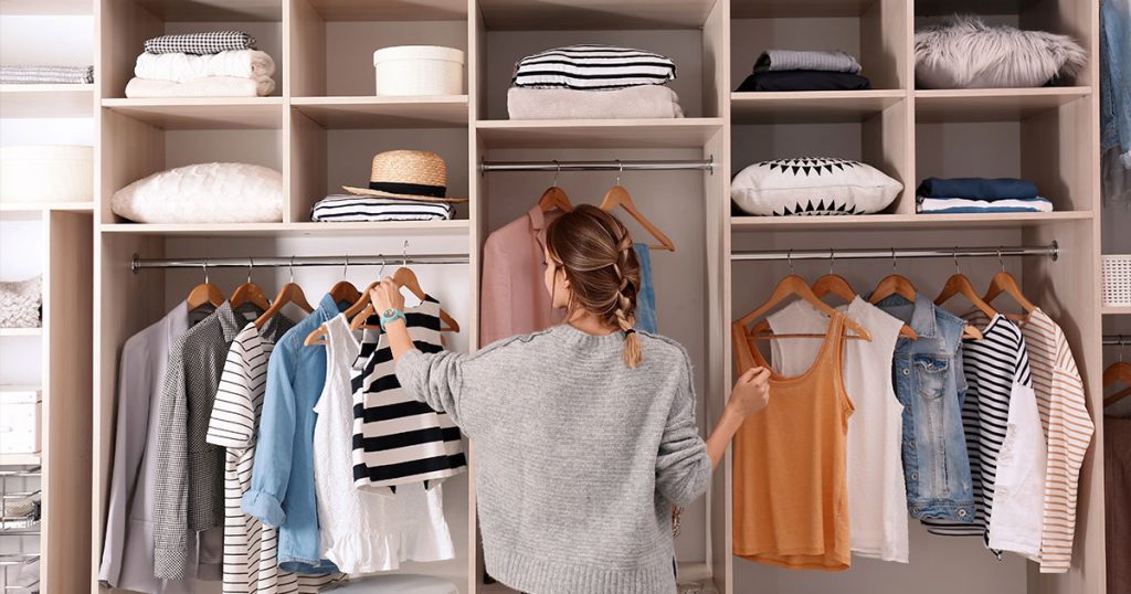 Woman organizing striped and casual clothes in a custom open wardrobe with built-in shelves and hangers